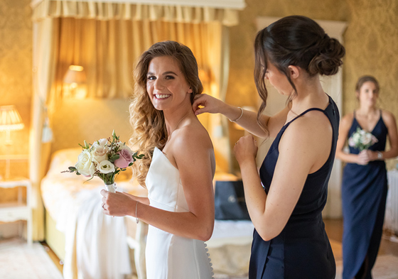 Bridesmaid helping bride get ready in bridal suite